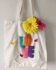 a white tote bag with the word love written on it and a yellow flower