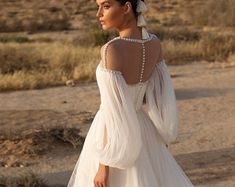 a woman in a white dress is standing on the dirt road with her back to the camera