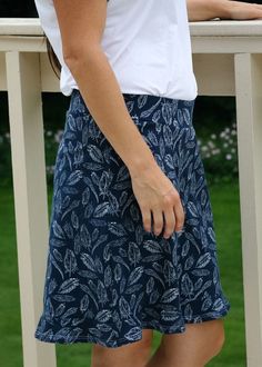 a woman standing next to a white fence with her hand on her hip wearing a blue skirt