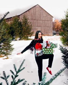 a woman holding a christmas present while standing in the snow with her arms outstretched out