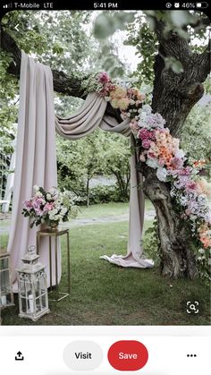 an outdoor wedding ceremony with pink drapes and flowers on the tree trunk, in front of a white gazebo