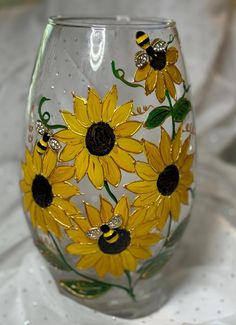 a glass with sunflowers painted on it sitting on a white tableclothed surface