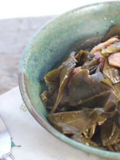 a bowl filled with greens and meat on top of a table next to a fork