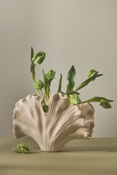 a white vase with green flowers in it on a table next to a gray wall