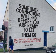 a man walking past a white building with graffiti on it's side and words written on the wall