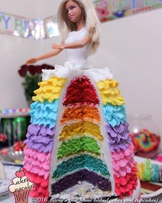 a barbie doll is standing on top of a cake with many layers and rainbow colors