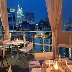 an outdoor dining area with tables and chairs overlooking the city skyline at night, lit up by candles