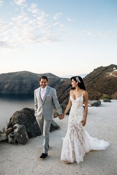 a bride and groom holding hands while walking on top of a mountain overlooking the ocean