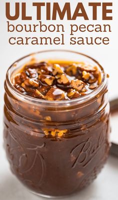 a jar filled with caramel sauce on top of a white table next to a spoon