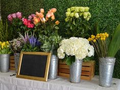 there are many different flowers in buckets on the table with a chalkboard next to them