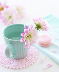 pink flowers are in a blue cup on a doily