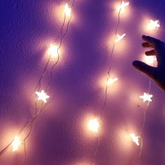 a hand is reaching up towards some lights on a wall that are glowing purple and white