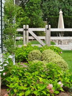 a garden with flowers and bushes in front of a fence