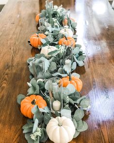 a wooden table topped with lots of pumpkins and greenery on top of it