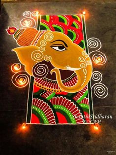 an artistic painting on the ground with candles lit up in front of it, depicting lord ganesha