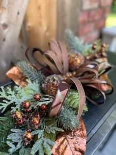 two wreaths with pine cones and evergreen leaves are on top of a bench in front of a brick wall