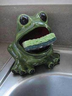 a green frog sitting on top of a metal sink