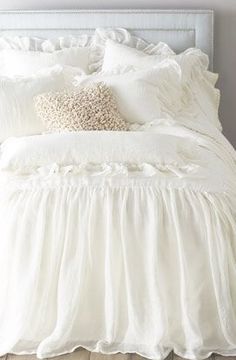 a white bed with ruffled bedspread and pillows