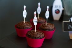 chocolate cupcakes with bowling pins on top are sitting in red paper cups that have the number forty written on them