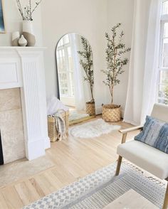 a living room with white walls and wooden floors, a fireplace, two chairs, rugs and a mirror on the wall