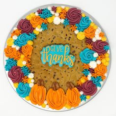 a cake decorated with flowers and the words give thanks written in blue, orange, and yellow frosting