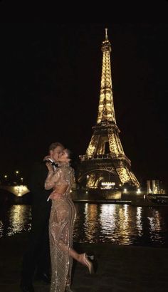 a man and woman standing in front of the eiffel tower, at night