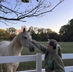 a woman petting a white horse on the nose while standing next to a fence