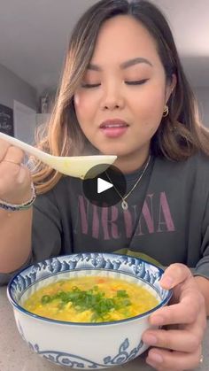 a woman is eating soup from a blue and white bowl