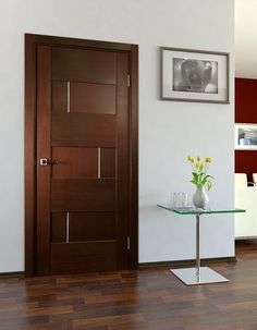 a vase with flowers on a glass table in front of a wooden door and white walls