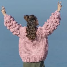 a woman wearing a pink sweater with her hands in the air