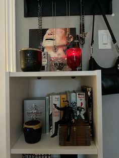 a shelf filled with books and jewelry on top of a white wall next to a black purse