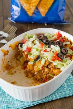 a white bowl filled with taco casserole next to a bag of tortilla chips