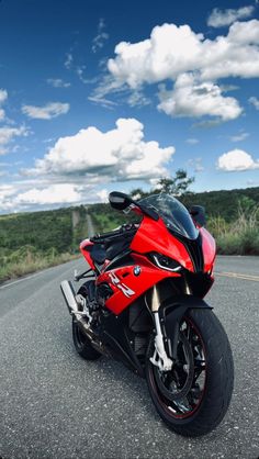 a red motorcycle is parked on the side of the road with clouds in the background