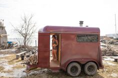 a woman is standing in the doorway of a tiny red trailer that has logs stacked on it