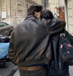 two people are walking down the street with their backs to each other and one person is wearing a leather jacket