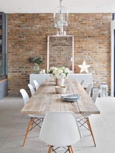 a dining room table with white chairs and a large brick wall in the back ground