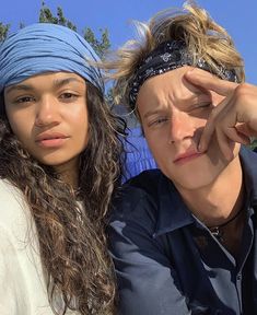 two people with bandanas on their heads posing for the camera, one is holding his head