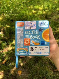 a hand holding up a blue sketch book with stickers on it's cover