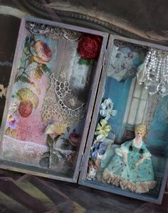 an open box with two dolls in it and some flowers on the inside, sitting next to each other