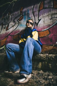 a young man sitting on the ground in front of a wall with graffitti