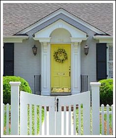 a white picket fence with a yellow door and wreath on the front entrance to a house