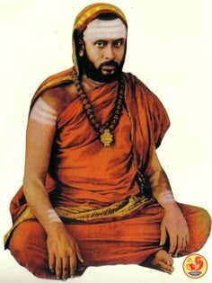 a man sitting on the ground wearing an orange outfit and headdress with beads around his neck