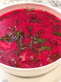 a white bowl filled with red soup and garnished with fresh herbs on top