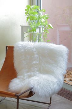 a chair that has some kind of white fur on it's back and is next to a potted plant