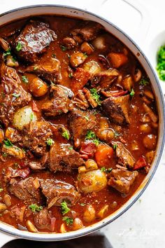 beef stew in a pot with potatoes and carrots on the side, garnished with parsley