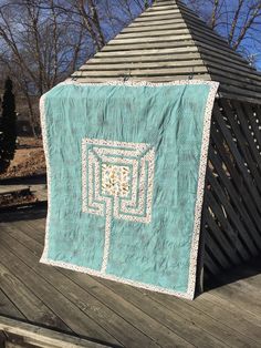 a teal colored quilt hanging on a wooden deck in front of a gazebo