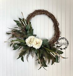 a wreath with white flowers and greenery hanging on the side of a wall next to a sign