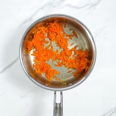 orange shredded carrots in a silver bowl on a white counter top with a metal spatula