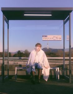 a man sitting on a bench in front of a bus stop with a sign above him