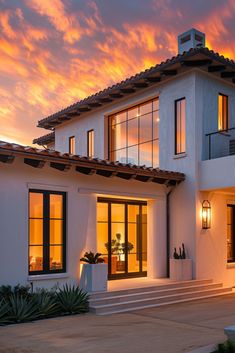 a white house with large windows and steps leading up to the front door at sunset